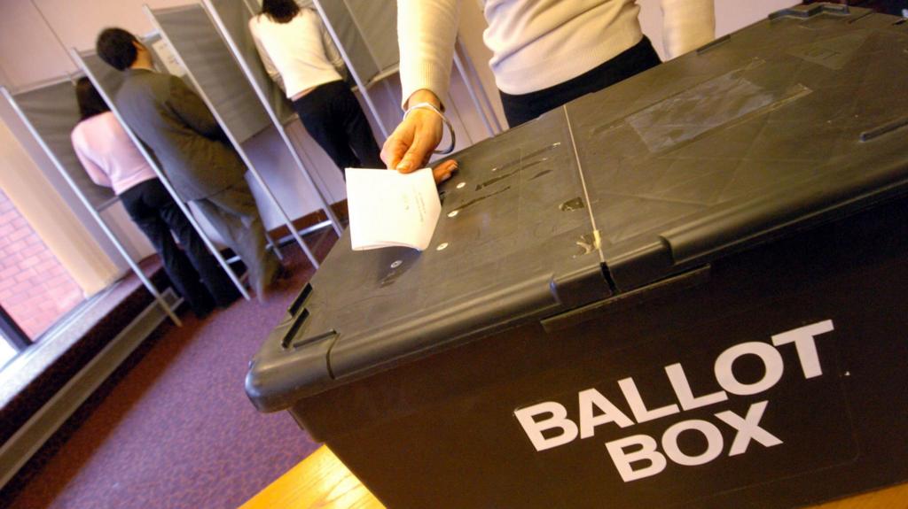 A black ballot box on a table with someone putting their ballot paper through the slot on top