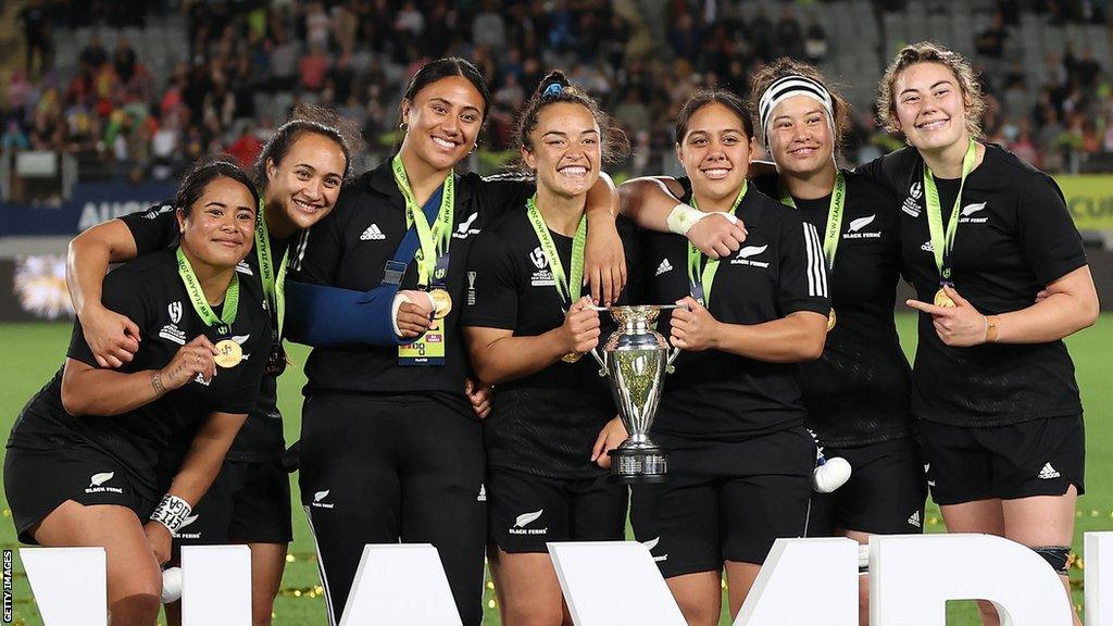 New Zealand women's rugby team smile as they hold up the World Cup trophy after beating England