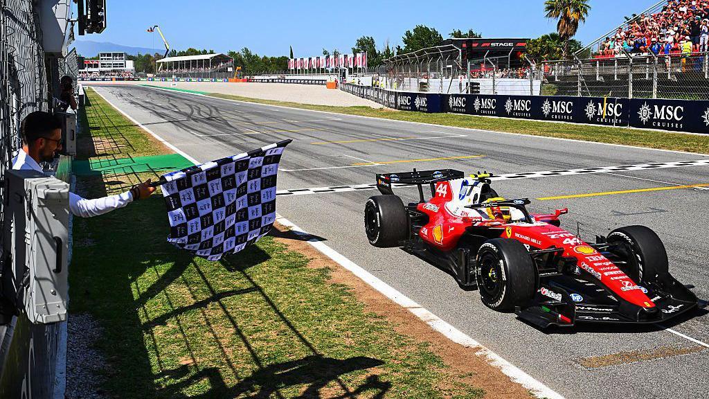 Lewis Hamilton crossing the line with Novak Djokovic waving the flag
