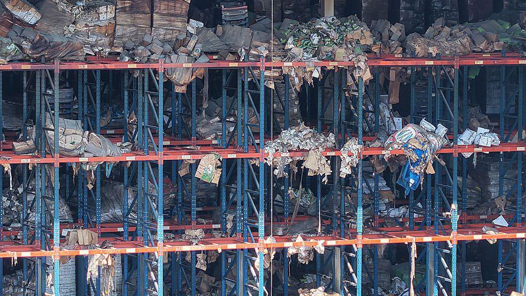 The scaffolding of a warehouse is strewn with rotting packages of food