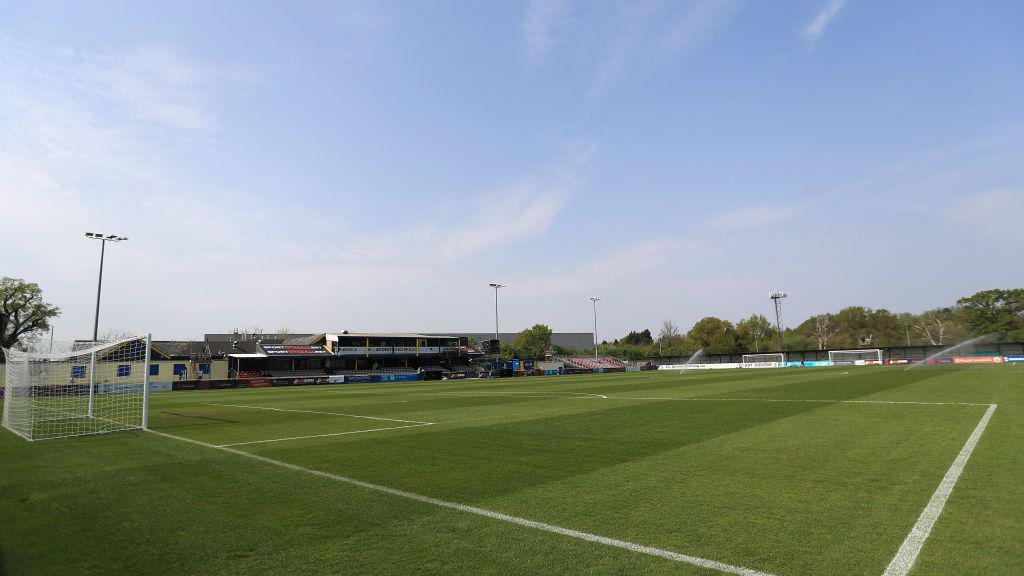 A football pitch, a goal is seen to the left and in the distance are some empty stands