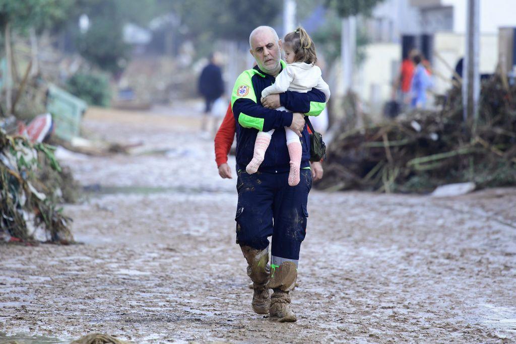 A Civil Protection member carries a child in a street covered in mud