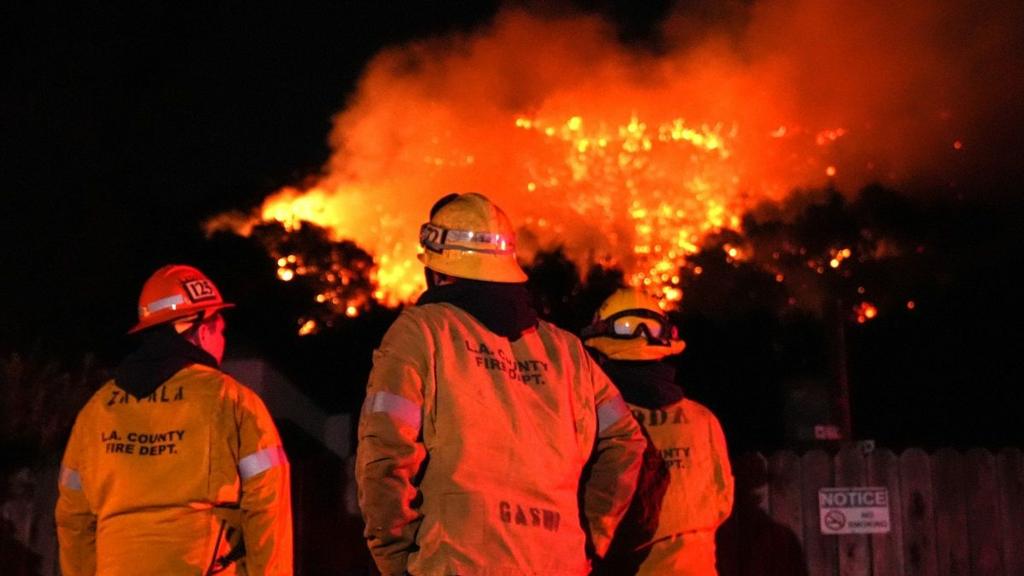 Three officials in hard hats watch a wildfire in the night