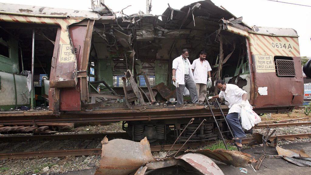 Investigators in white clothes collect forensic evidence from one of the trains  where the bombs exploded. The part of the coach can been seen ripped apart.
