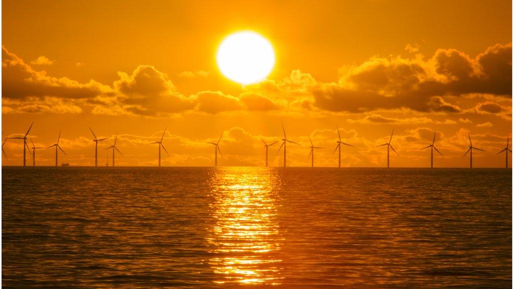 Orange sun over wind turbines on the sea