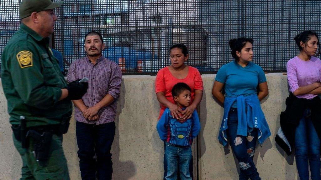 Migrants, mostly from Central America, wait to board a van which will take them to a processing center