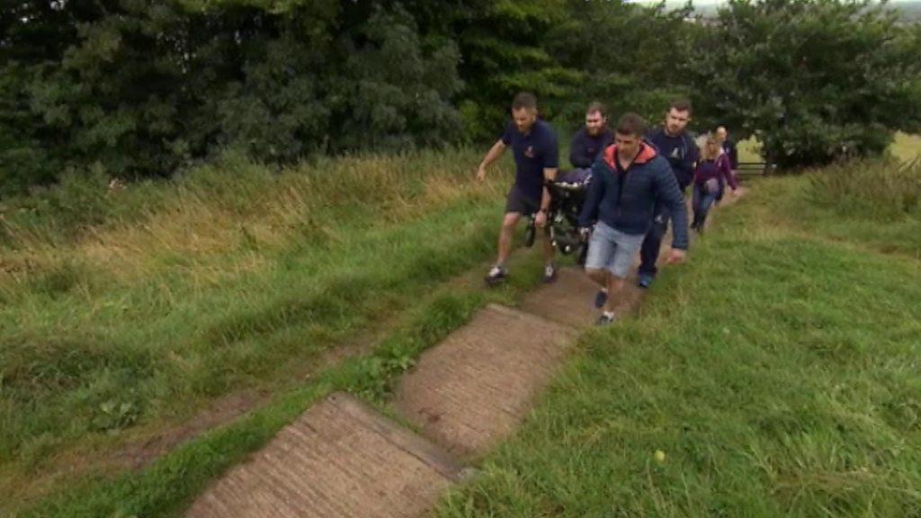 Rugby players carry wheelchairs up the Tor