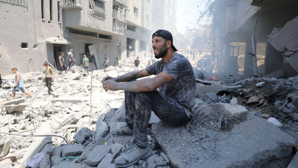 A Palestinian man sits on rubbles of destroyed buildings following the Israeli attacks on Al-Shati refugee camp in Gaza City