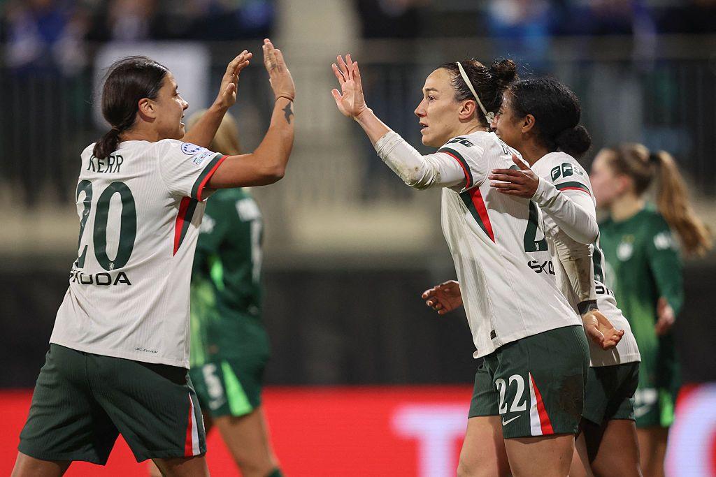Sam Kerr and Lucy Bronze, in predominantly white shirts, celebrate with raised hands to each other as if to give a high-five salute