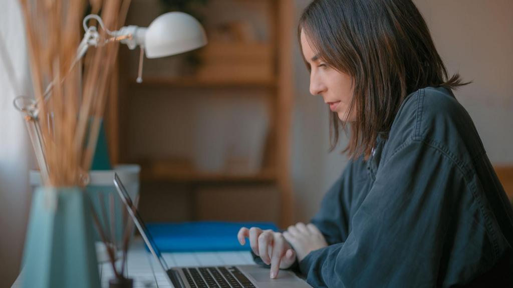 Side view of woman in black shirt sitting at her desk while using a laptop.