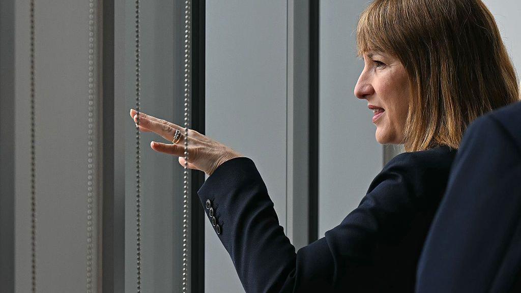 Chancellor Rachel Reeves sitting down near a window with her hand stretched in front of her.