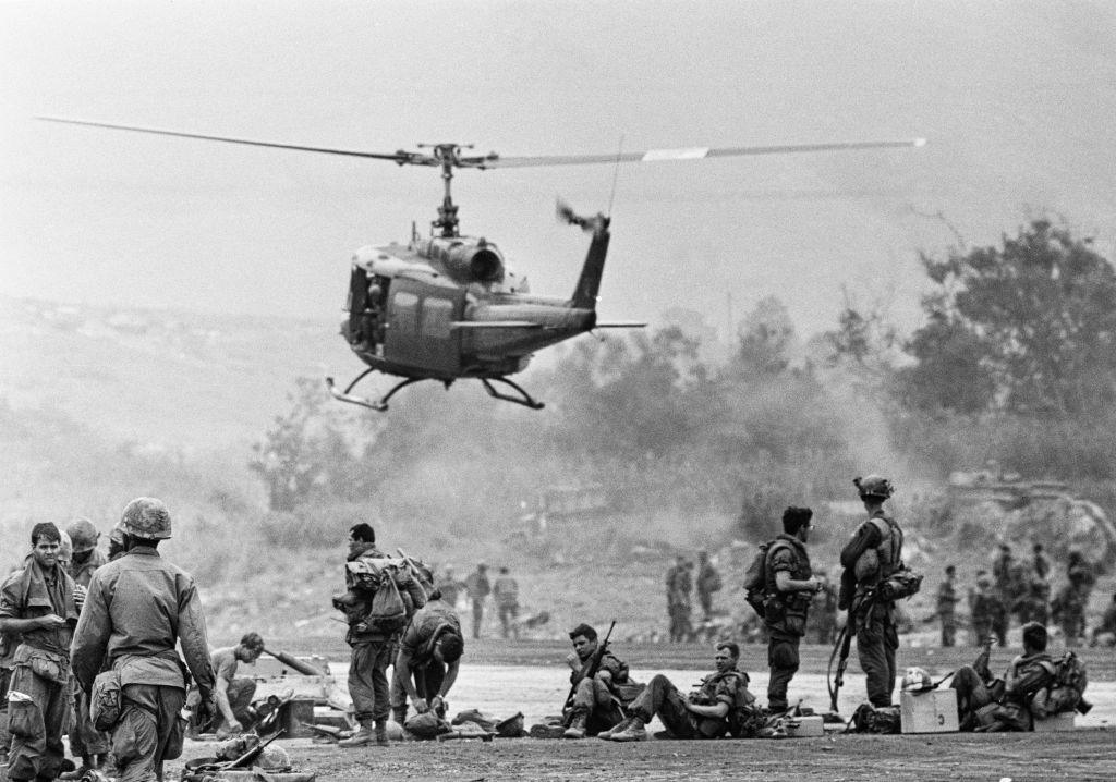 A helicopter hovers above soldiers in Vietnam jungle. 