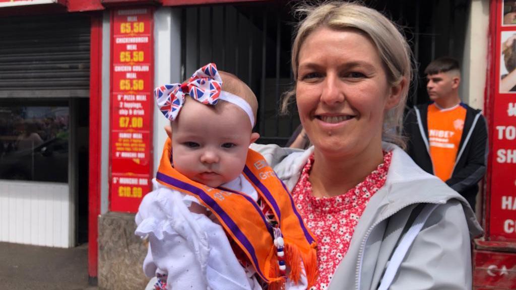 Mother and baby wearing orange sash in Coleraine