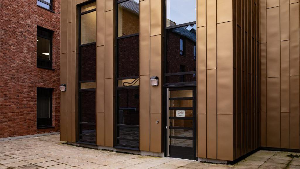 The front of a red brick building with a brown and black entranceway