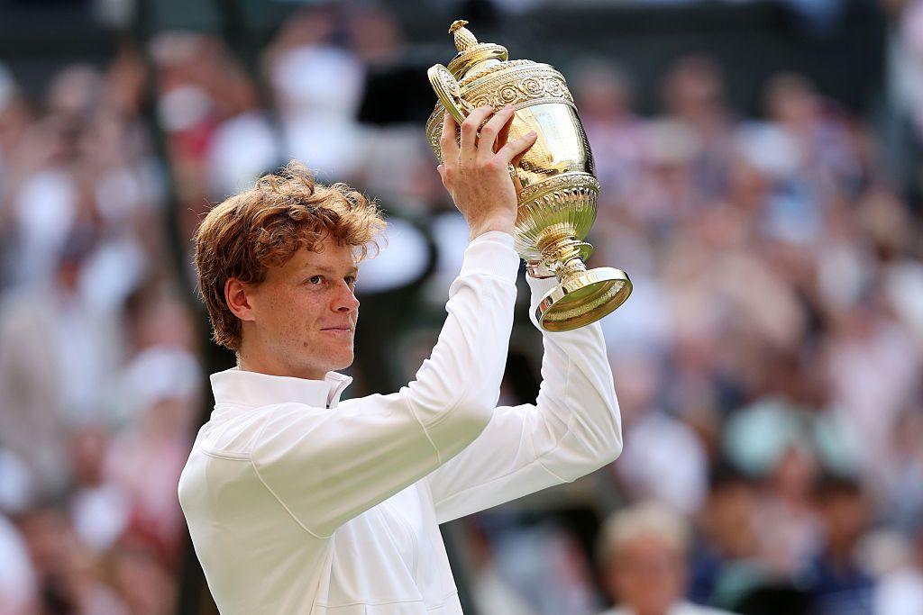 jannik sinner smiling while holding the wimbledon men's singles trophy aloft in front of a crowd of people in centre court