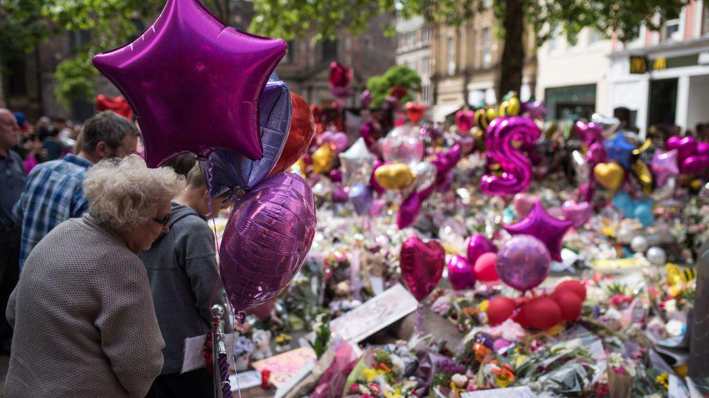 Tributes to the victims of the Manchester arena attacks are shown filling the city centre in 2017, with members of the public looking at a huge number of flowers and pink balloons filling a city centre street.