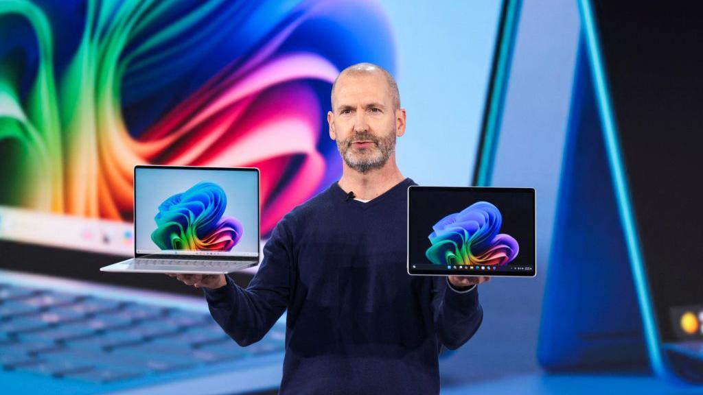 Microsoft executive Brett Ostrum holds laptops during a presentation at the firm's showcase in May.