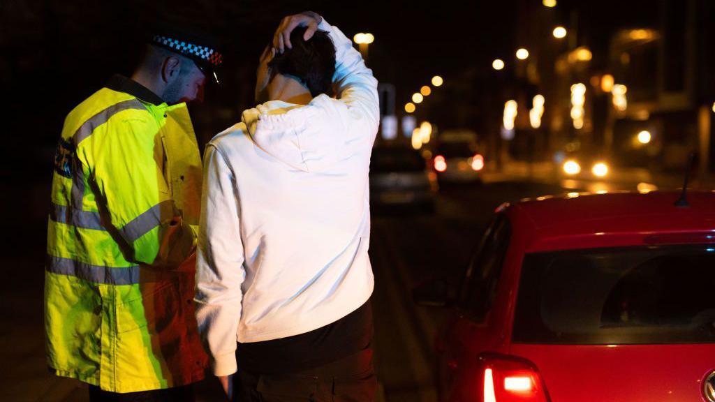 Police breathalyse a man at the side of the road next to a red car