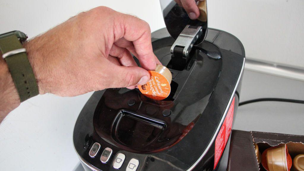 A man's hand is inserting a coffee pod into a coffee machine.