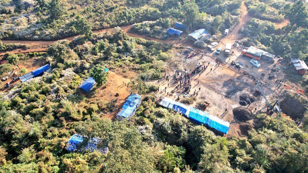 A patch of land with greenery, dotted by camps with blue, plastic sheds at the rescue site.