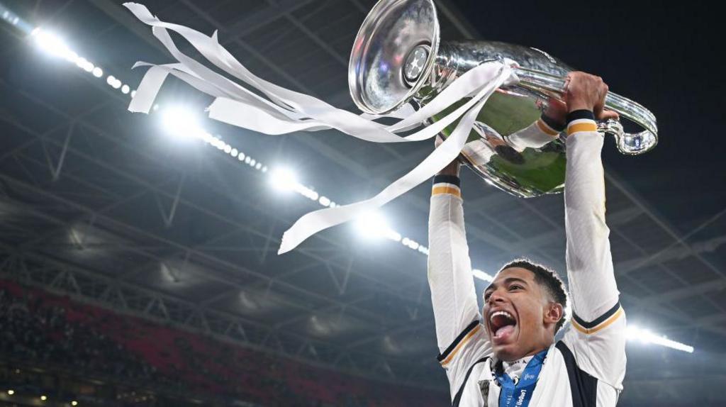 Jude bellingham holding up the Champions League trophy for Real Madrid