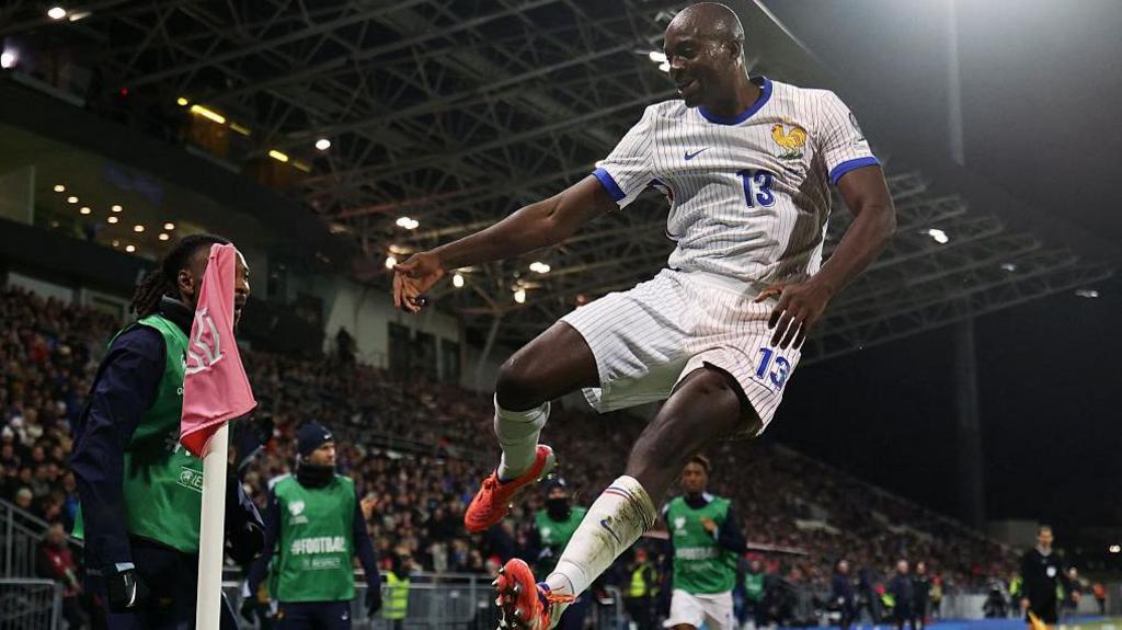 Jean-Philippe Mateta jumps into the air by the corner flag, smiling