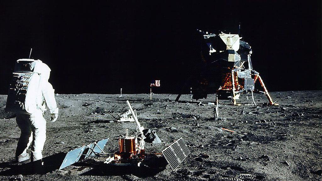 Astronaut Edwin E. Aldrin Jr. stands near a scientific experiment on the lunar surface wearing a space suit.