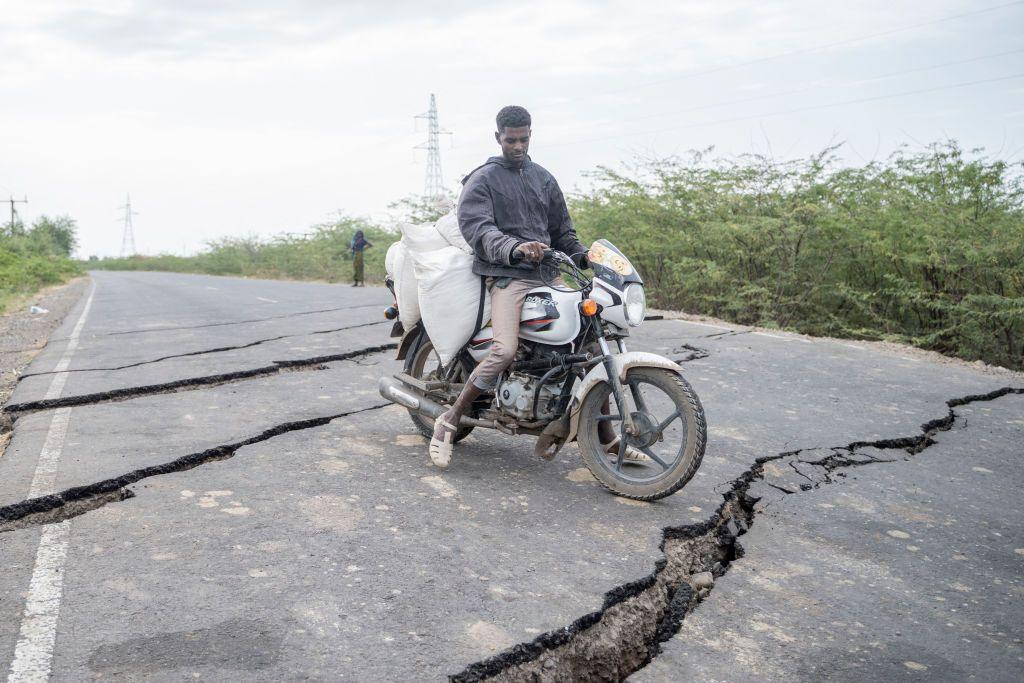 A man rides a motorbike along a road that is scarred with huge cracks across it.