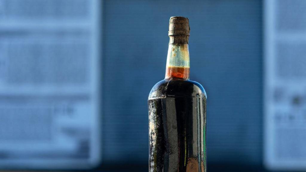 A glass bottle containing a dark brown liquid with a dark brown bottle top