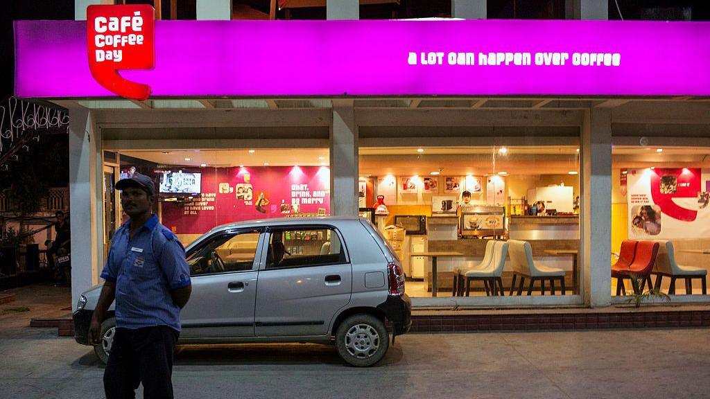 A Hindustan Petroleum Corp. employee stands in the gas station forecourt in front of a Cafe Coffee Day store, operated by Amalgamated Bean Coffee Trading Co., in Jaipur, Rajasthan, India, on Monday, Oct. 13, 2014