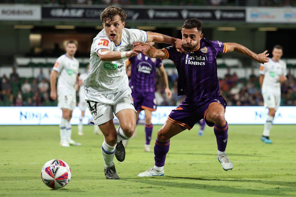 Callan Elliot in a white strip battles with another footballer in a purple top to secure possession of the ball while a number of team mates and opponents look on.