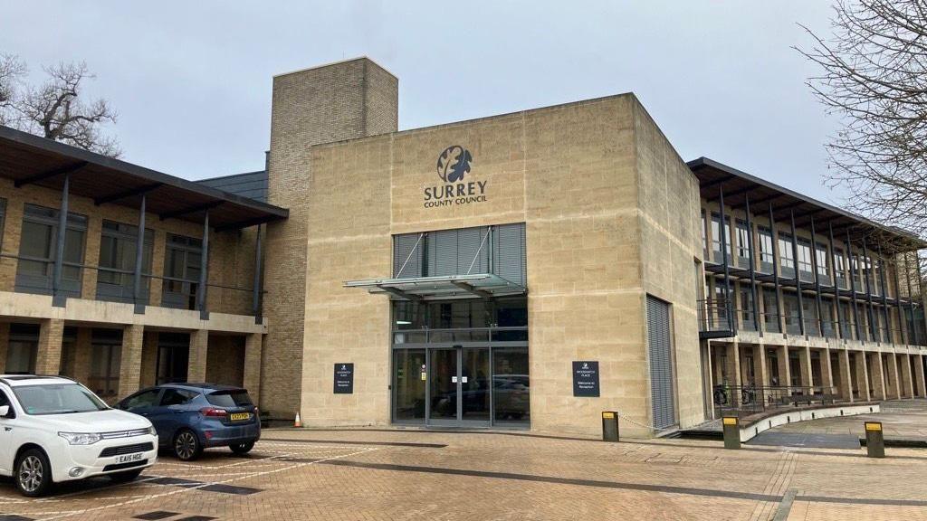 The front entrance to Surrey County Council offices at Woodhatch Place in Reigate. Two cars are parked outside the building.