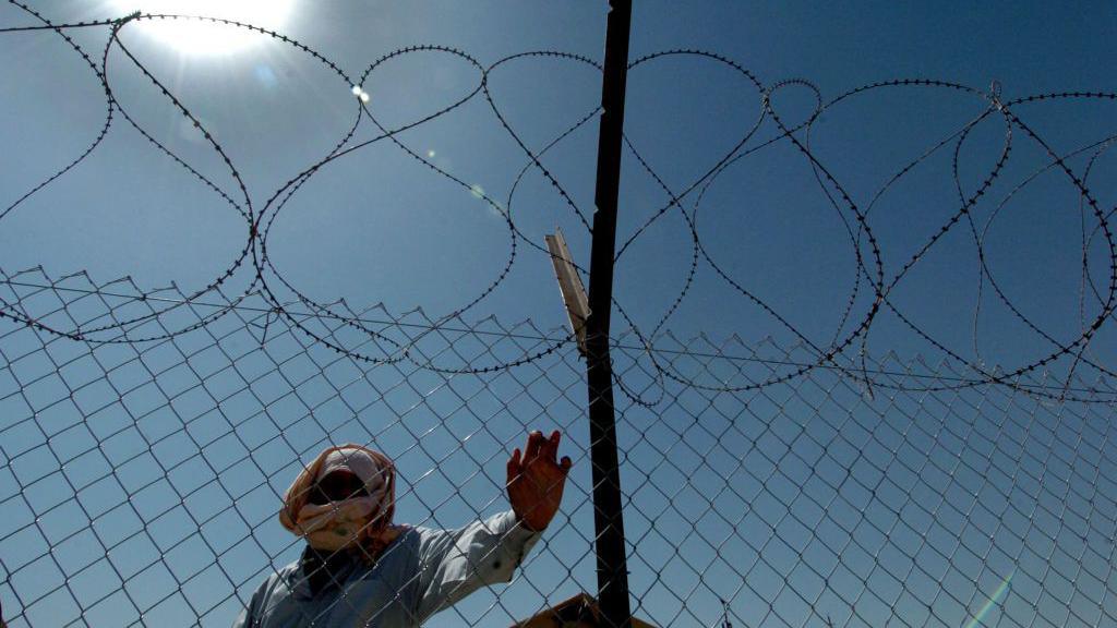 An Iraqi detainee holds the fence as he watches the release of prisoners leaving the Abu Ghraib prison on the outskirts of Baghdad, 16 September 2004