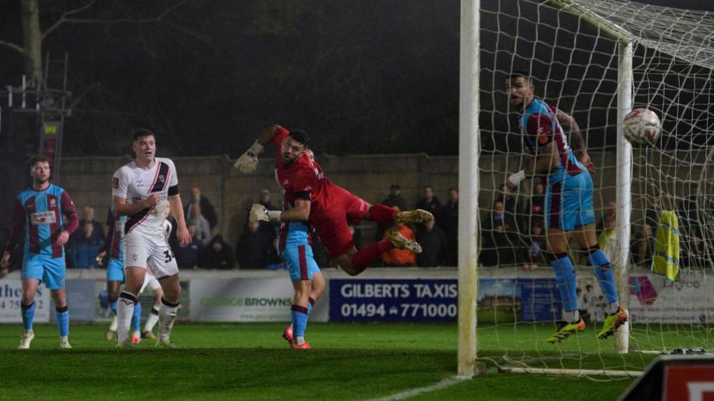 Chesham United goalkeeper Ben Goode looks on as Jack Moylan's strike flies into the back of the net