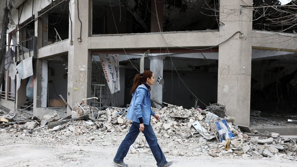 A woman walks next to the Qatari Al-Araby TV and business building damaged by a strike, as the U.S.-Israeli conflict with Iran continues, in Tehran, Iran