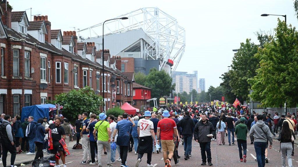 A crowd of fans walk to Old Trafford down Sir Matt Busby Way