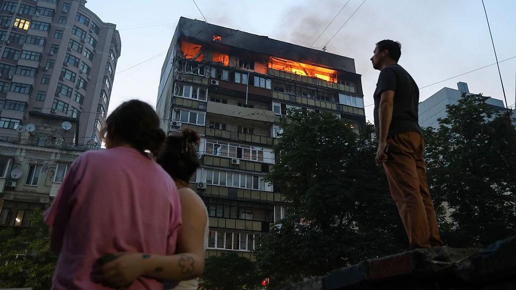 People look at burning apartments in a high-rise residential building hit by Russian shelling on July 10, 2025 in Kyiv, Ukraine.