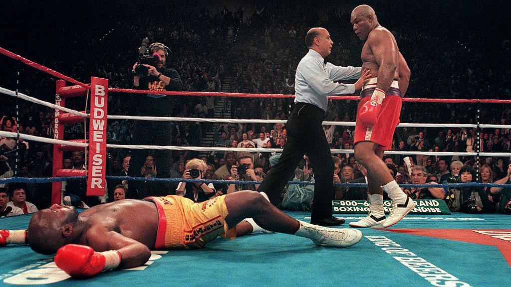 Michael Moorer lies on the canvas as George Foreman is ushered away by the referee