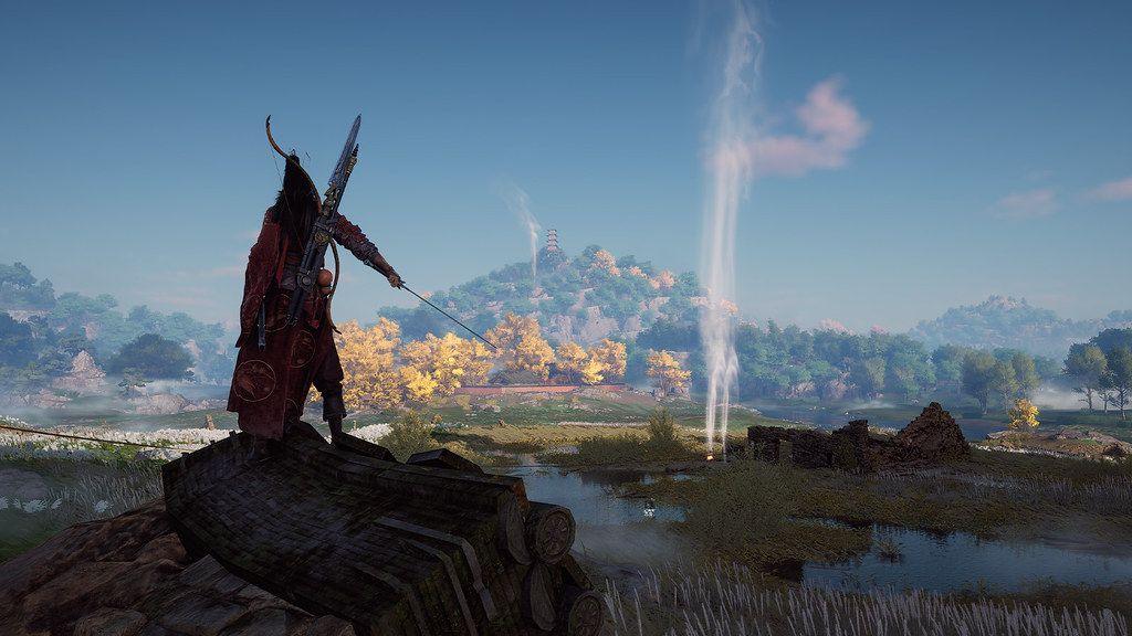 A character seen in silhouette holds a thin katana-like sword out at their side as they stand on a rock overlooking a vast rural landscape. There are small rustic settlements in the foreground, turning into hilly, forested landscape in the distance