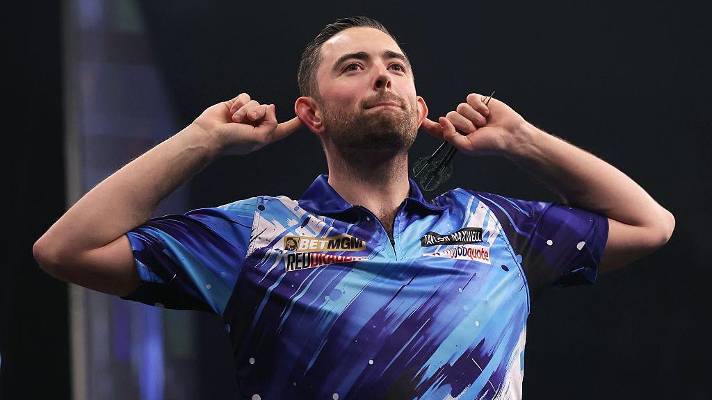 Luke Humphries cups his ears in celebration during a match