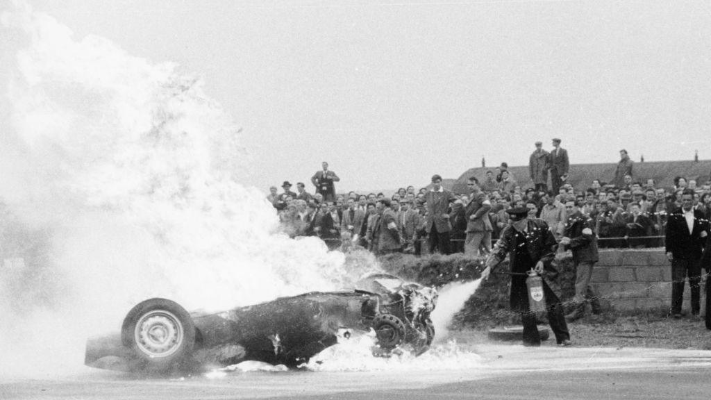Tony Brooks' car on fire at the British Grand Prix, Silverstone, Northamptonshire, 1956. Brooks' BRM spun and overturned on lap 40 and caught fire. He was thrown clear of the car and fortunately avoided serious injury. A marshall tries to extinguish the fire. 