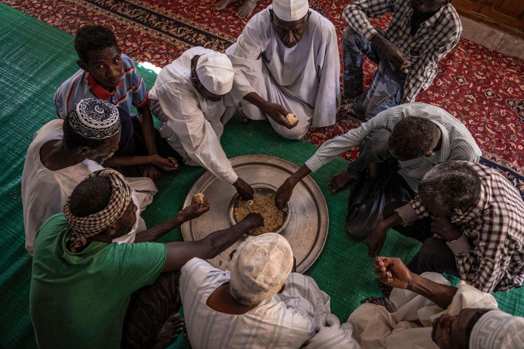 Men sit on the floor covered with mats around a dish placed on a silver platter. They  are sharing the food, eating with their hands, in Omdurman, Sudan - Friday 1 November 2024