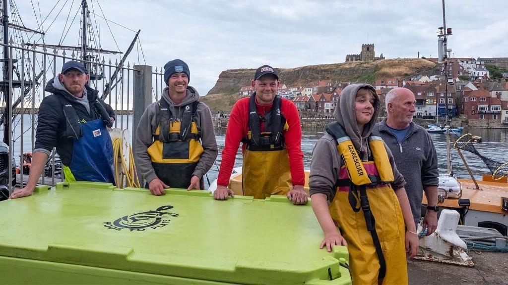 Four men and one woman, all wearing commercial fishing clothing, stand next to a freezer box where the bluefin tuna is being stored.