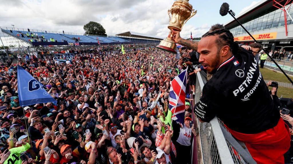 Lewis Hamilton holds aloft the winner's trophy to the fans below after winning in 2024, his first grand prix victory since the 2021 season