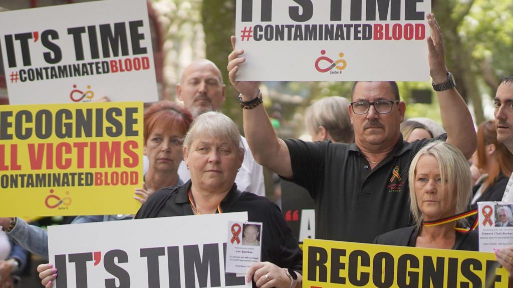 Campaigners hold posters reading 'It's time #contaminated blood' posters have white and yellow backgrounds