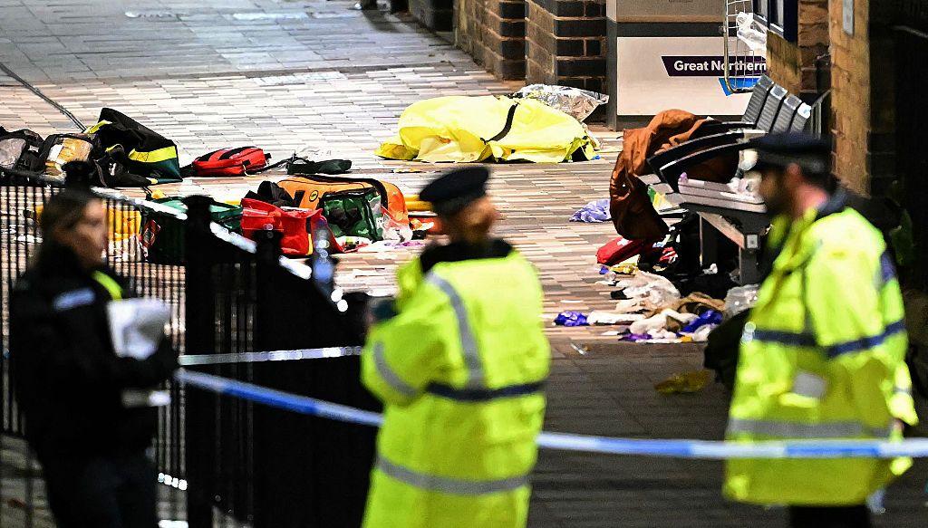 Police officers in hi-vis jackets stand in front off a cordoned off area where bags and medical supplies are strewn across the ground
