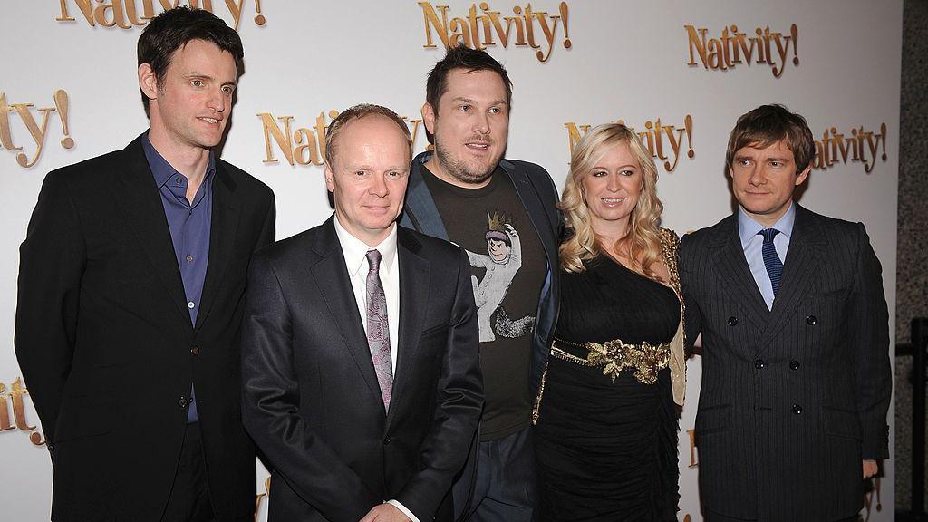 Jason Watkins, Marc Wootton, and Martin Freeman are all dressed in suits. Debbie Isitt is dressed in a black dress with gold belt. They are all standing in front of a large white background that says the word "Nativity" on it 