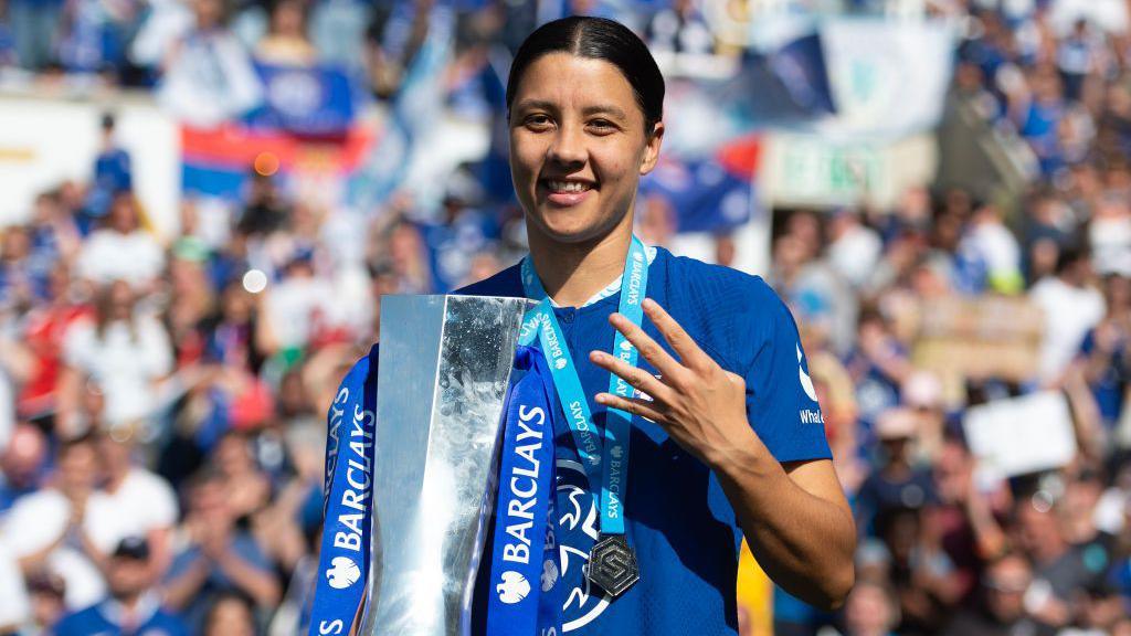 Chelsea striker Sam Kerr holds up four fingers alongside the Women's Super League trophy