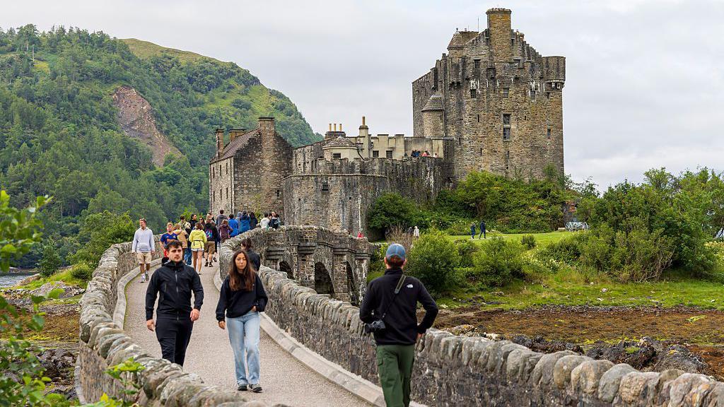 Luchd-turais a' coiseachd thar drochaid Chaisteil Eilein Donnain