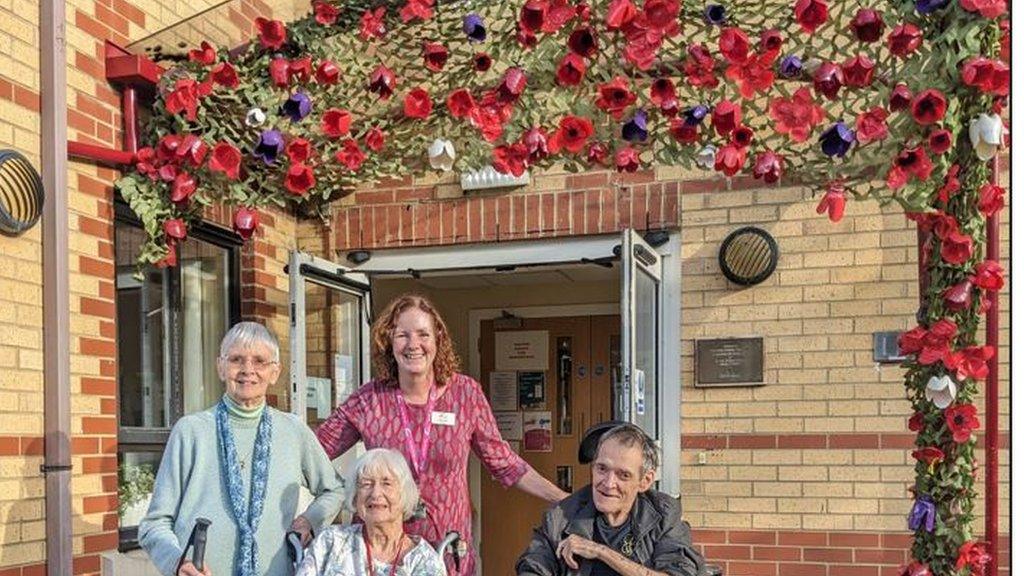 MHA Brookfield residents and a carer smile in front of the poppy display